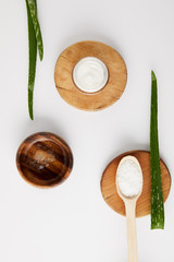 elevated view of organic cream in container and spoon with salt on wooden slices, aloe vera leaves and wooden bowl with aloe vera juice on white surface