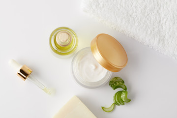 Fototapeta na wymiar top view of organic cream, cosmetic oil and soap, pipette, towel and aloe vera slices on white surface