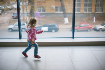a little girl runs around the new large apartment near a panoramic window