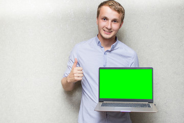 young guy in shirt, holding laptop with green screen in front of him