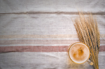 Foam beer in a mug and rye ears on a burnt wooden table background.