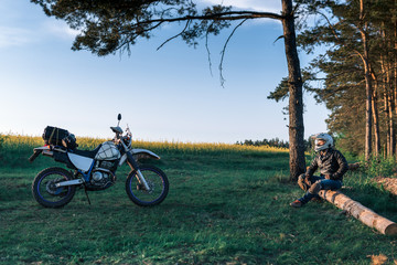 motorcyclist with his bike, sunset outdoor view, green grass and pine forest, off road motorcycle adventure, enduro, rider, dual sport road trip, travel concept