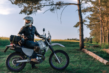 Fototapeta na wymiar motorcyclist with his bike, sunset outdoor view, green grass and pine forest, off road motorcycle adventure, enduro, rider, dual sport road trip, travel concept