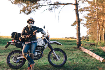 motorcyclist with his bike, sunset outdoor view, green grass and pine forest, off road motorcycle adventure, enduro, rider, dual sport road trip, travel concept