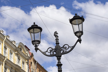 Fototapeta na wymiar Patterned decorative street lamp with horse head and two lamps on blue sky background with clouds in St. Petersburg