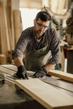 Skilled carpenter cutting a piece of wood in his woodwork workshop