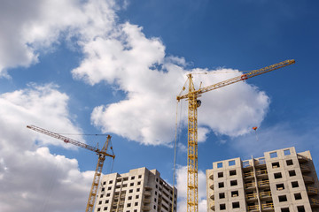 Fototapeta premium Tower cranes and unfinished multi-storey high near buildings under construction site in the sunny day with beautiful clouds