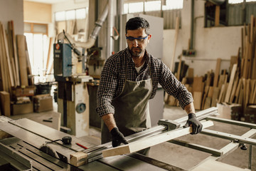 Skilled carpenter cutting a piece of wood in his woodwork workshop