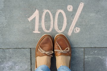 Female feet with text 100 percent written on grey sidewalk