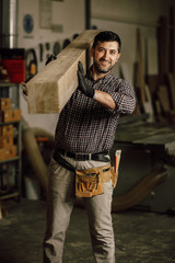 Portrait of a smiling carpenter holding wood planks in a construction site