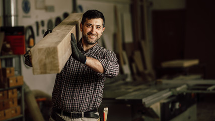Portrait of a smiling carpenter holding wood planks in a construction site