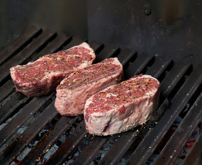 Raw steaks with spices on hot grill.