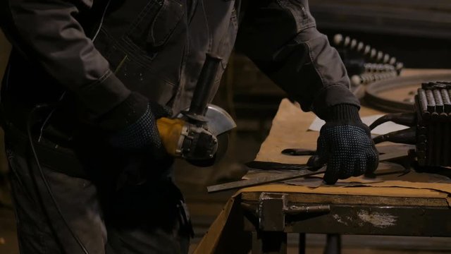 Professional blacksmith sawing metal with hand circular saw at forge, workshop. Handmade, craftsmanship and blacksmithing concept