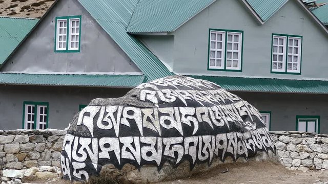 Traditional prayer stone with an inscription "om mane padme hum", the main mantra of Buddhism, on the background of buildings in the Himalayas mountains.