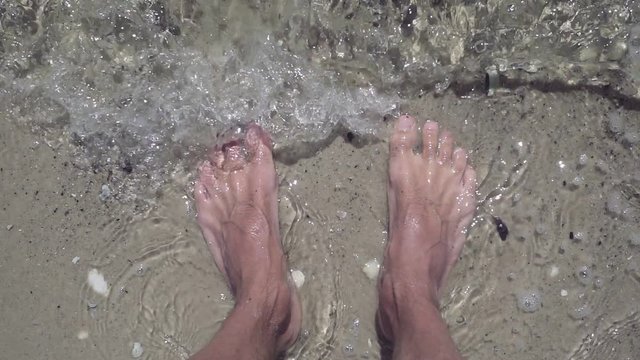 Closeup of male feet in clear sea water on beach.