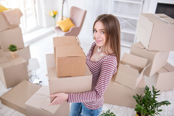 Unpacking actively. Charming young woman holding two boxes and smiling at the camera before proceeding to open them