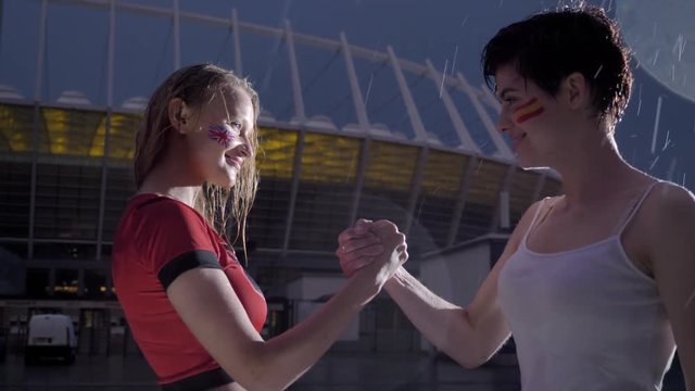 Champions League, two young girls football fans in the rain are shaking hands, confrontation concept 60 fps