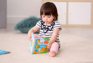 Cute baby girl with book sitting on floor at home