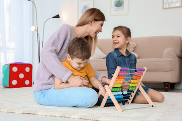 Nanny and little children playing with counting frame at home