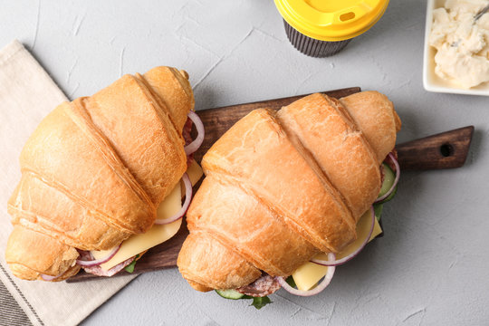 Tasty croissant sandwiches with salami on grey background