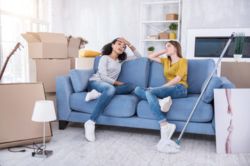 Feeling fatigue. Charming young girls sitting on the sofa and wiping sweat off their foreheads,...