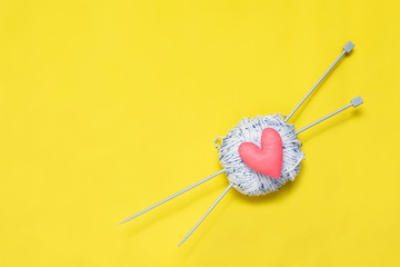 Top view of yarn and red felt heart on yellow background, love to knit image concept