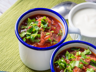 Russian beetroot soup borscht in enamel mugs on green cloth