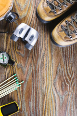 Hiking or travel equipment with boots, compass, binoculars, matches on wooden background. Active lifestyle concept