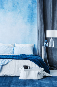 Blue watercolor paint on the wall in modern bedroom interior with a double bed and grey curtain