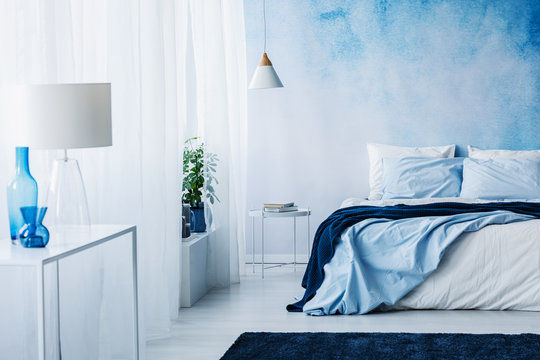 Relaxing bedroom interior with white and blue decorations, double bed and wallpaper