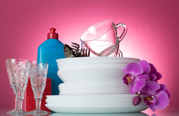 Plates, Cutlery, crystal glasses and bottle with detergent on pink