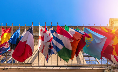 Different flags of many countries on building facade, sky background. Bottom view - obrazy, fototapety, plakaty