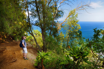 Young male tourist hiking on beautiful Pololu loop trail located near Kapaau, Hawaii, that features beautiful wild flowers and stunning views to the Pololu Valley