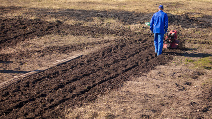 Worker with a machine cultivator digs the soil in the garden