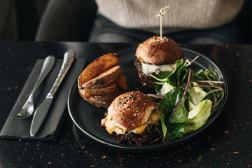 Delicious burgers with lettuce and fries on black plate in cafe