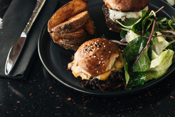 Delicious burgers with lettuce and fries on black plate in cafe