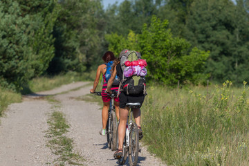 Fototapeta na wymiar Two pretty girls cycling in the wild nature on dirt road. Bikes cycling girl. Girl rides bicycle. Blue backpack
