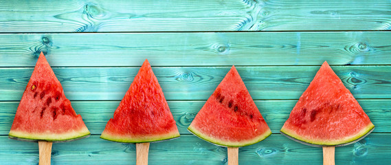Four watermelon slice popsicles on panoramic blue wood background, fresh summer fruit concept