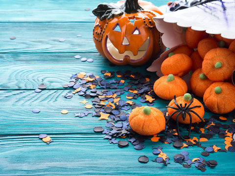 Halloween trick or treat still life on dark green. Toy pumpkin, sweets, marshmalllow, confetti. Holiday mood background