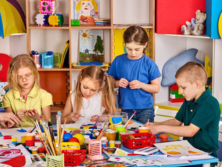 Fototapeta premium Plasticine modeling clay in children class. Teacher teaches kids together play dough and mold from plasticine in kindergarten or preschool. Group of four people. Learning in game.