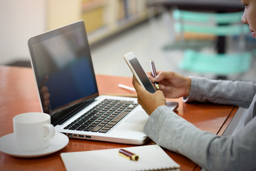 The hand of Beautiful Asian businesswoman using a mobile phone with a laptop in the office. Business, Financial and Technology Concepts.