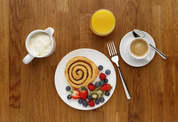 A Cinnamon Swirl breakfast with fruit, coffee and orange juice, shot on a wooden background, from above.