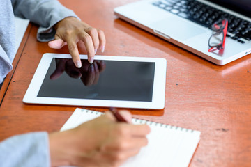 Beautiful Asian businesswoman is using and touching a tablet. At the same time, he wrote the report with a pen on the table to her office. Finance, Banking and Technology Concepts.
