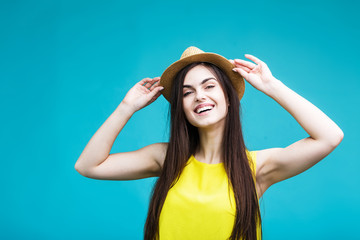Obraz na płótnie Canvas Beautiful smiling brunette girl dressed in yellow shirt toches her hat before blue background