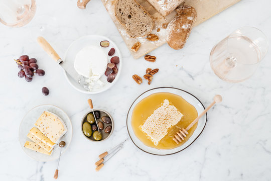 Cheese platter with olives, nuts, grapes and honey on a marble table.