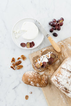 Cheese platter with bread, nuts and grapes on a marble table.