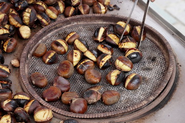 Vendor toasts chestnuts on the metal sheet şn the street.