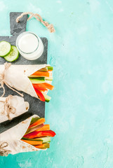 Summer healthy snack, Mexican style tortilla sandwich wraps assorted colorful fresh vegetable sticks (celery, rhubarb, pepper, cucumber and carrot) with yoghurt sauce dip light blue background