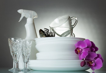 Clean plates and Cutlery, glass cups and crystal glasses, Orchid flower, on grey
