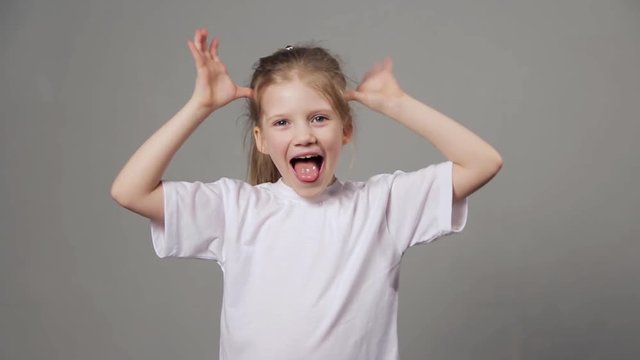 Cute young girl playing the ape. Funny girl showing grimaces over grey background.